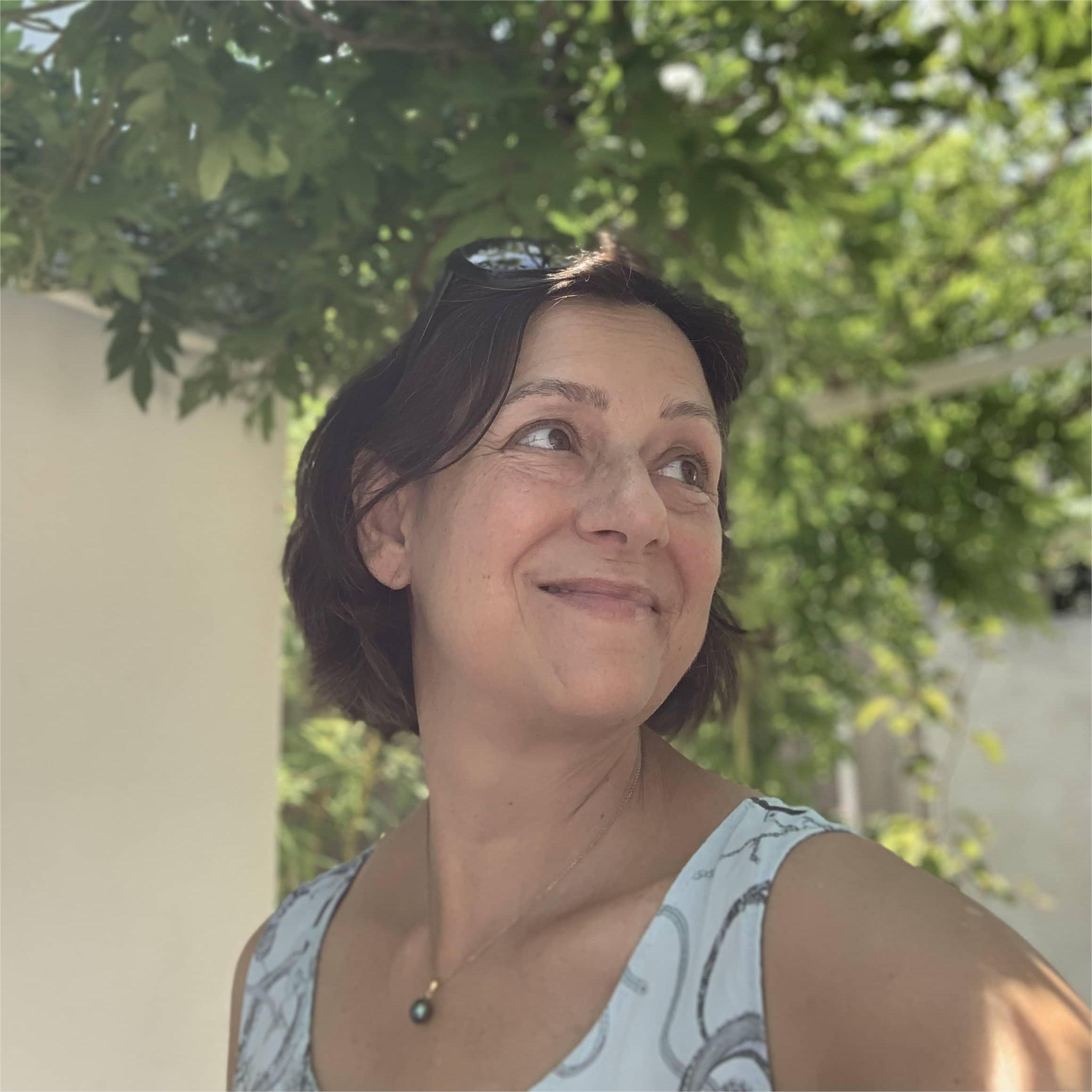 Portrait de Régine Lamure Zapata, consultante en parentalité, souriante sous un arbre, regard tourné vers la lumière.